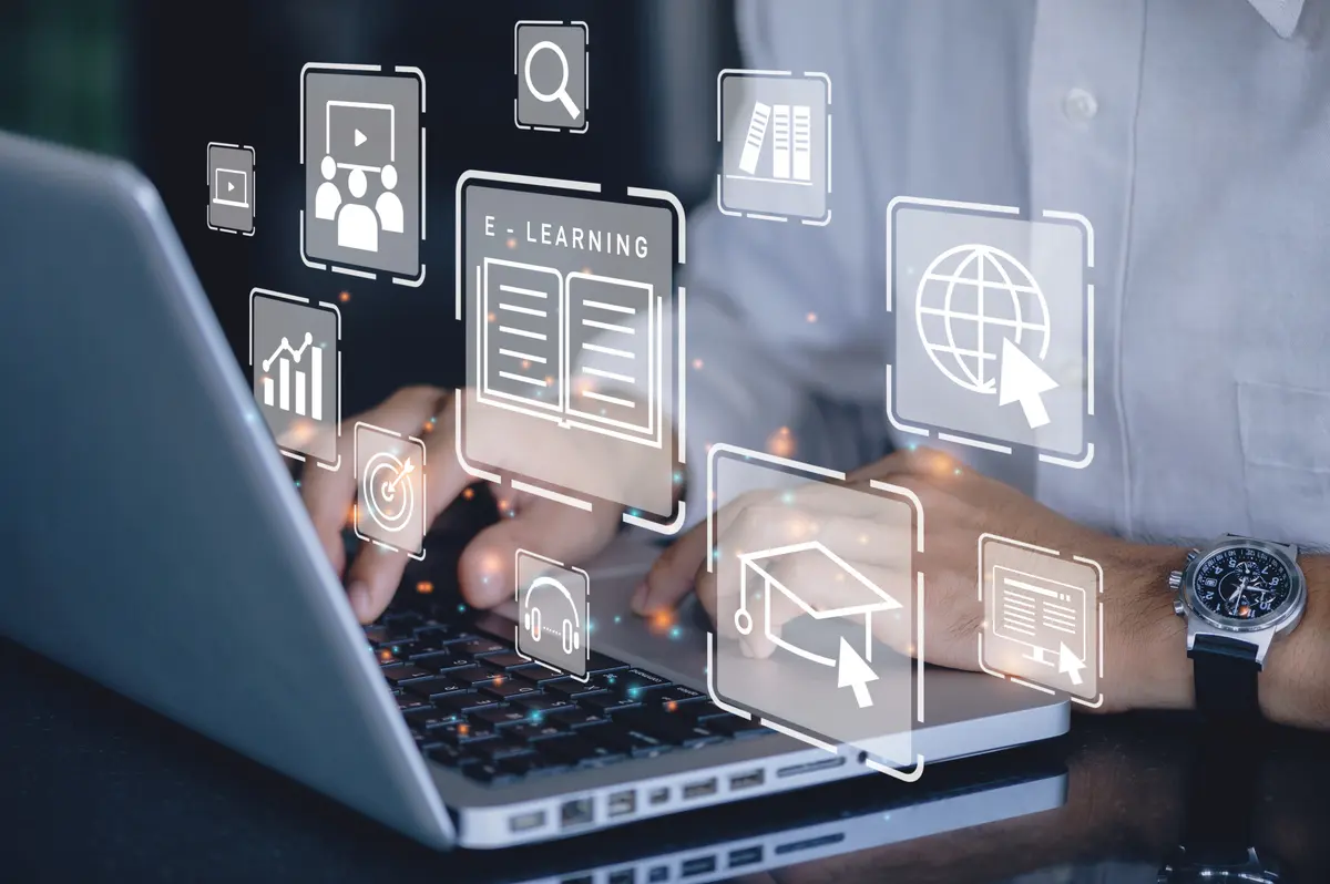 Person types on a laptop surrounded by floating holographic e-learning and education icons