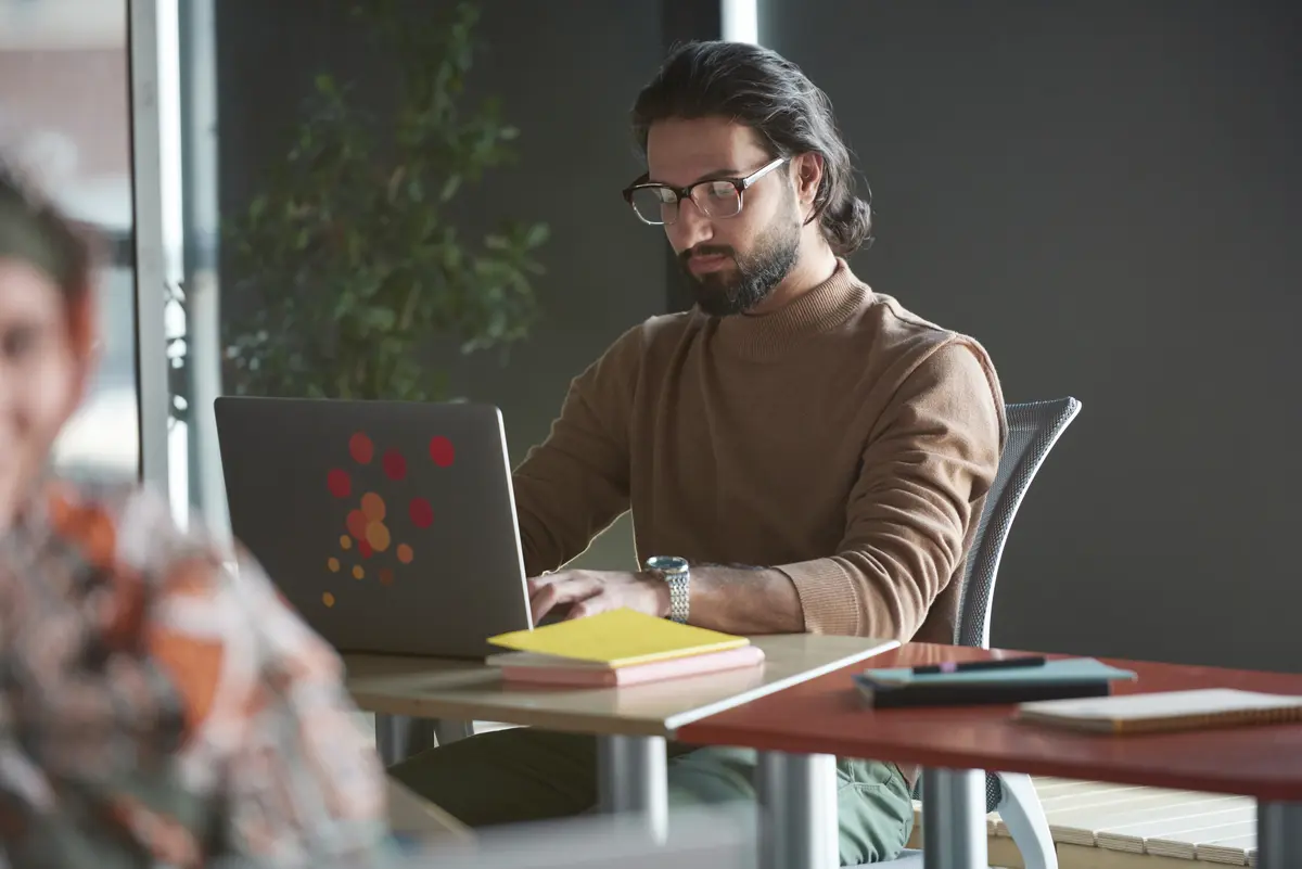 Man wearing glasses and brown sweater working on a laptop at a modern office desk